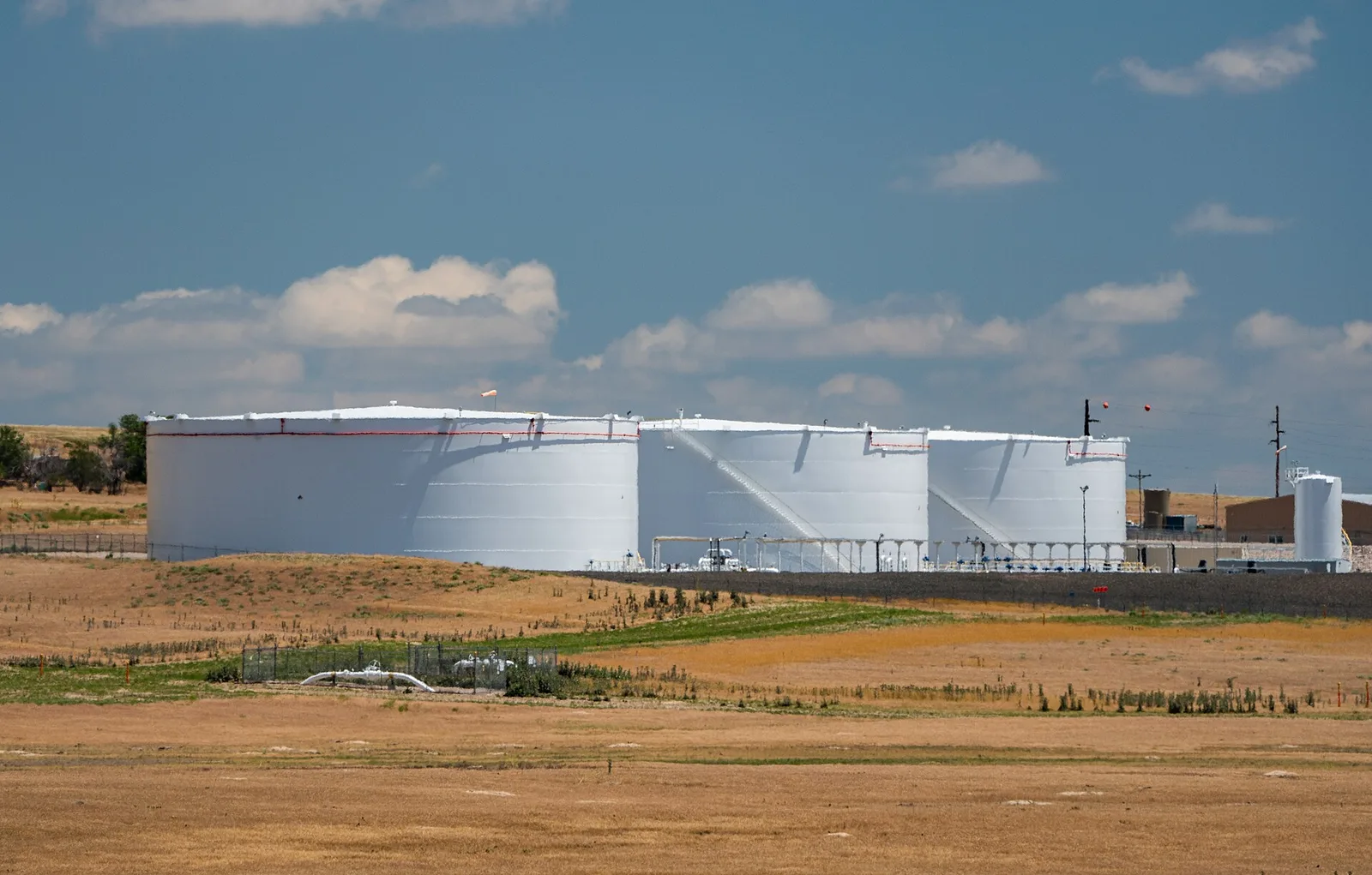 White fuel storage tanks on dry grassland under a wide sky